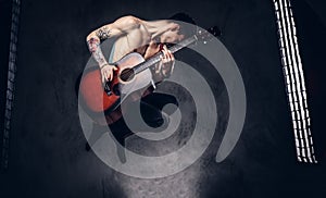 Handsome shirtless young musician playing guitar while jumping.