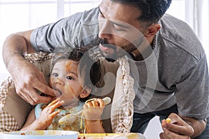 Handsome single young father feeding spaghetti for his mixed race daughter while baby girl sitting on high chair. Infant cute