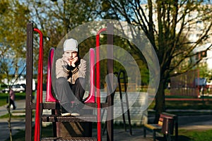 A handsome six year boy is bored sitting on the playground. Place for text