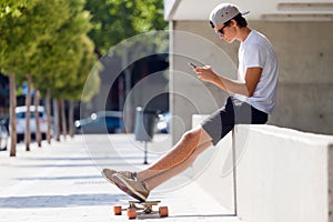 Handsome skater boy using his mobile phone in the street.