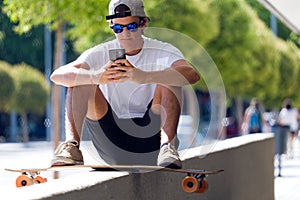 Handsome skater boy using his mobile phone in the street.