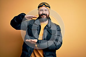 Handsome skier bald man with beard skiing wearing snow sportswear and ski goggles gesturing with hands showing big and large size