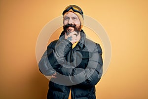 Handsome skier bald man with beard skiing wearing snow sportswear and ski goggles looking confident at the camera smiling with