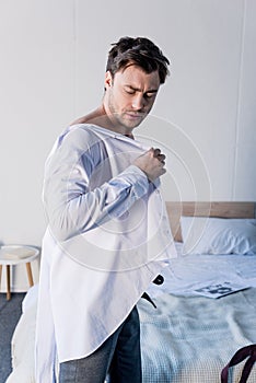 Handsome sleepy man dressing white shirt in bedroom at home.