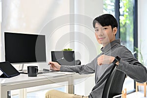 Handsome Asian male graphic designer or program developer sits at his desk in modern office