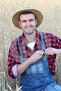 Handsome smiley farmer standing in a wheat field fixing his overalls