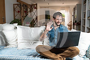 Handsome and smiley man with blue shirt, attending a video call or virtual meeting on his laptop