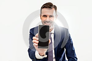 Handsome smiling businessman showing phone with blank black screen to the camera. Man holding smart mobile cell phone in hand