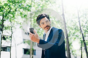 Handsome smiling businessman using smartphone for listining music while walking in city park.Horizontal,blurred