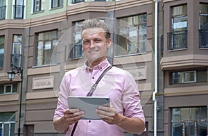 Handsome smiling freelancer estate businessman with pad tablet in hand standing over building background. Broker with