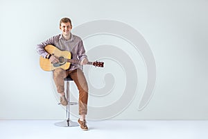 Handsome smiling guitarist play music siting on chair