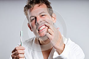 handsome smiling guy brushing tooth, wearing bathrobe, isolated on gray studio background