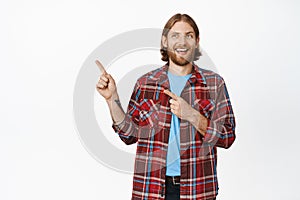 Handsome smiling hipster guy, blond caucasian man with beard, looking and pointing fingers left at promo banner, showing