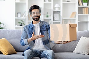 Handsome Smiling Indian Man Pointing At Cardboard Box With Delivery At Home