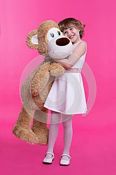 Handsome smiling little girl hugging a toy bear on an isolated pink background