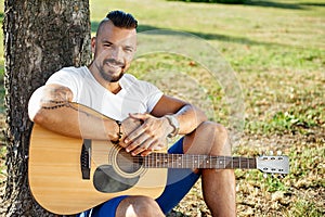 Handsome smiling man with acoustic guitar ina summer park