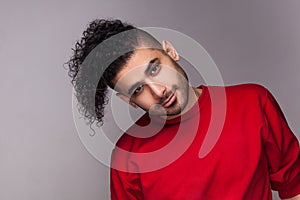 Handsome smiling man with curly hair, tilts his head aside, looking at camera with calm expression.