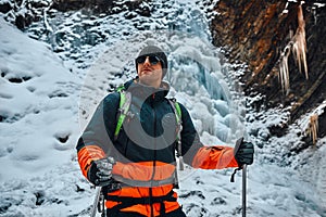 Handsome smiling man dressed in warm sportswear and sunglasses holding trekking poles and smiling. Hiking, trekking, sports and