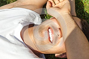 Handsome smiling man lying on the grass covering his eyes with hand against the sun