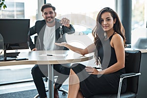 Handsome smiling man manager giving car keys after holding successful deal to his beautiful woman client at dealership