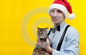 Man in red santa hat, blue shirt and black suspender holding cute brown tabby cat and looking at camera