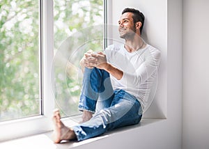 Handsome smiling man relaxing on window sill