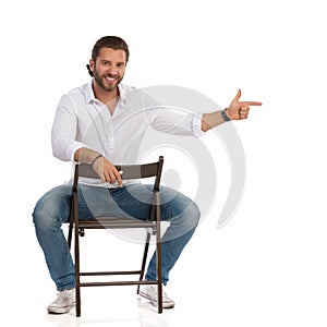 Handsome Smiling Man Is Sitting On A Chair, Looking At Camera And Directing