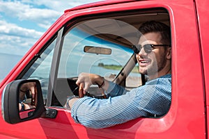 handsome smiling man in sunglasses driving car during