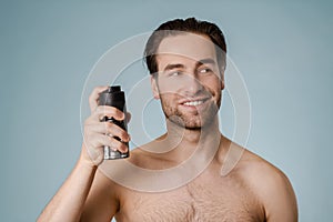 Handsome smiling nude man spraying deodorant