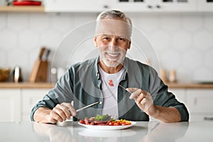Handsome Smiling Senior Man Eating Tasty Meal In Kitchen At Home