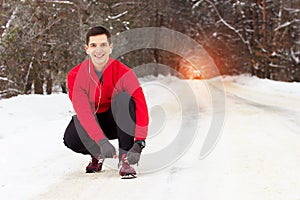 Handsome smiling sportsman in red sweater ties shoelaces of his sneakers. Outdoor activity.
