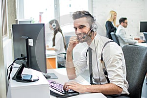 Handsome smiling young call center agent speaking with costumer in call center.