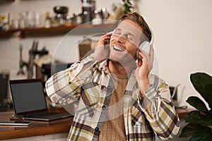 Handsome smiling young man, digital nomad, sitting in co-working open space, working in coffee shop, singing and