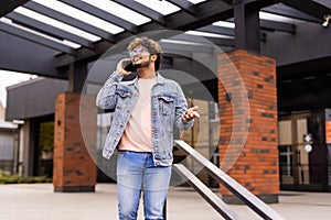 Handsome smiling young man dressed casually spending time outdoors at the city, talk mobile phone while walking down stairs