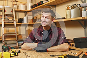 Handsome smiling young man working in carpentry workshop at wooden table place with piece of wood