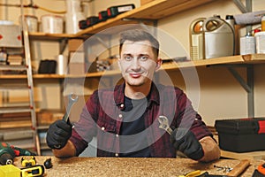 Handsome smiling young man working in carpentry workshop at wooden table place with piece of wood