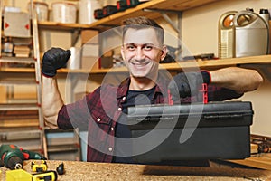 Handsome smiling young man working in carpentry workshop at wooden table place with piece of wood