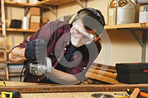 Handsome smiling young man working in carpentry workshop at wooden table place with piece of wood