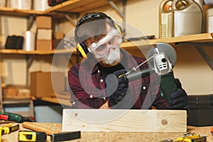 Handsome smiling young man working in carpentry workshop at wooden table place with piece of wood