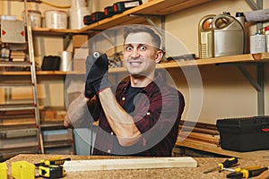 Handsome smiling young man working in carpentry workshop at wooden table place with piece of wood