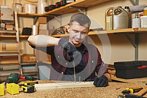 Handsome smiling young man working in carpentry workshop at wooden table place with piece of wood