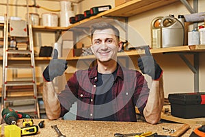 Handsome smiling young man working in carpentry workshop at wooden table place with piece of wood