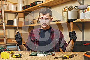 Handsome smiling young man working in carpentry workshop at wooden table place with piece of wood