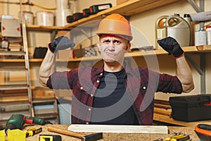 Handsome smiling young man working in carpentry workshop at wooden table place with piece of wood