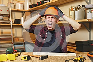 Handsome smiling young man working in carpentry workshop at wooden table place with piece of wood