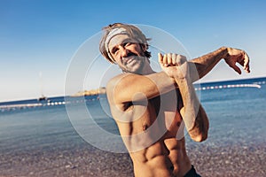 Handsome sports man doing stretching before run at the beach