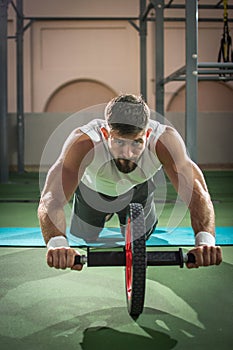 Handsome sportsman doing ab wheel rollout exercise and looking forward while working out at gym