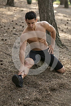 Handsome sportsman doing stretching exercises with legs in the park. Healthy lifestyle concept. Vertical view