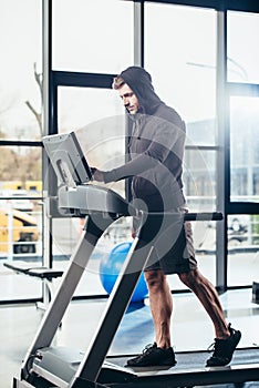 handsome sportsman in hoodie exercising on treadmill photo