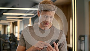 Handsome sportsman using smartphone in sport club. Bodybuilder standing at gym.